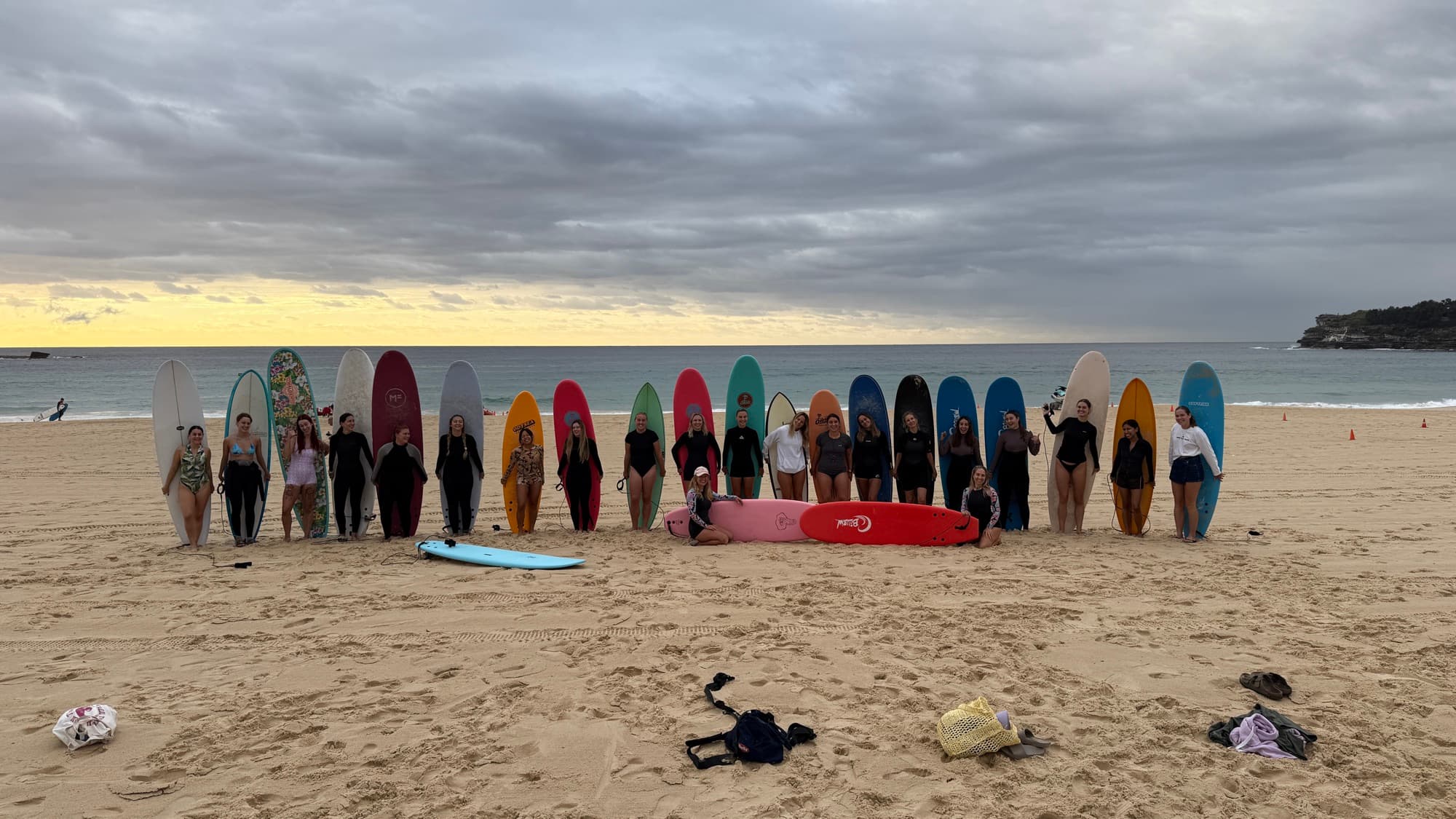 Women from the Bondi Surf Girls community lined up on the sand with colourful softboards at Bondi Beach